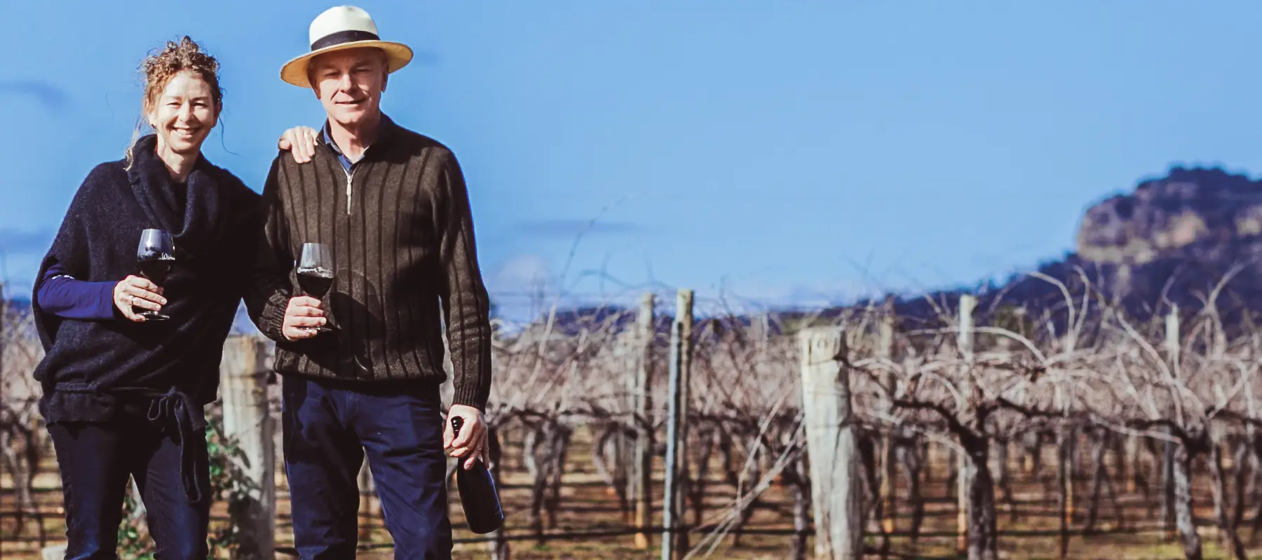 Susan and Adam standing in the vineyard with glasses of wine